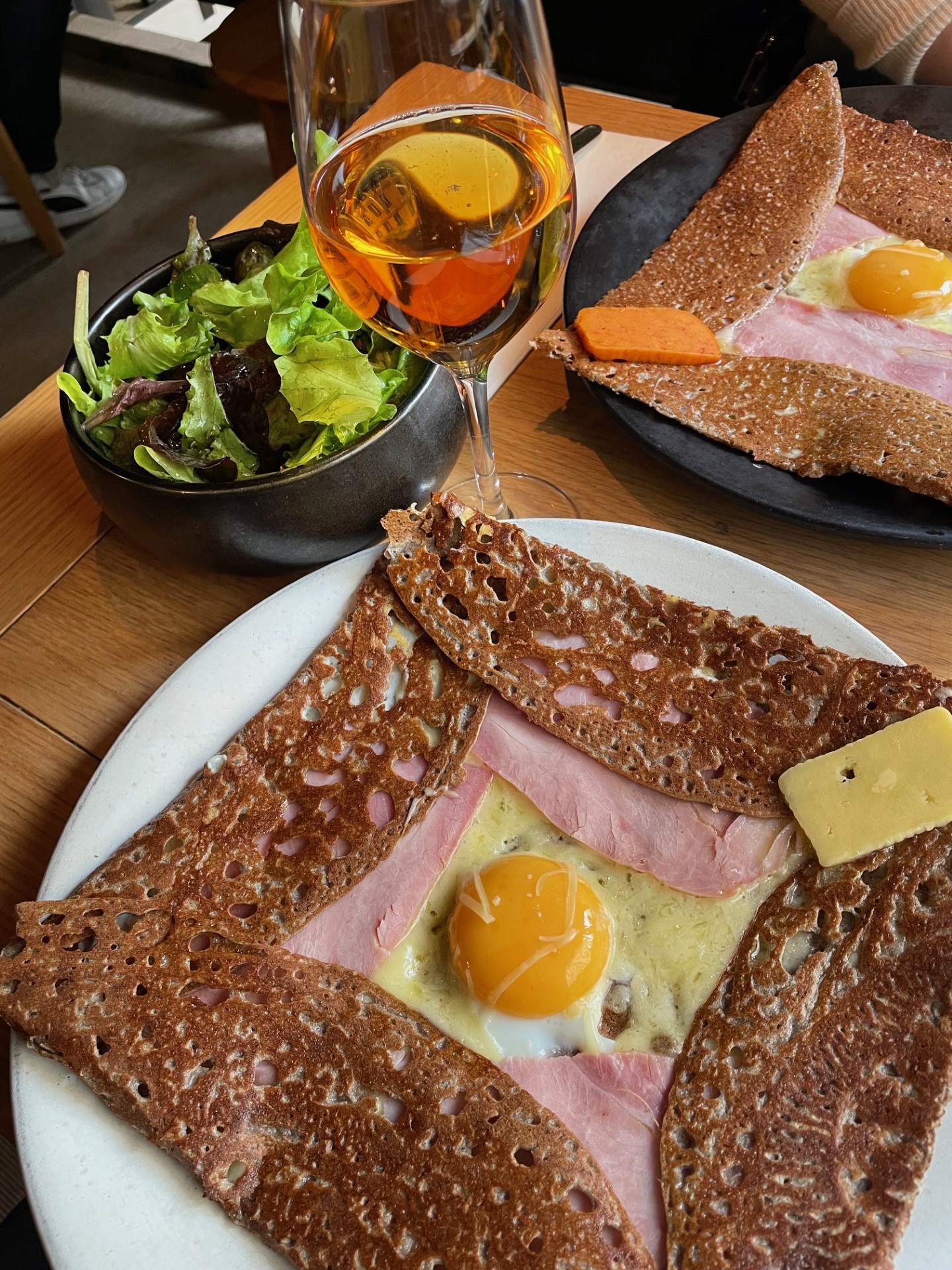 Close up picture of a savory ham and cheese crepe with a glass of cider and salad.